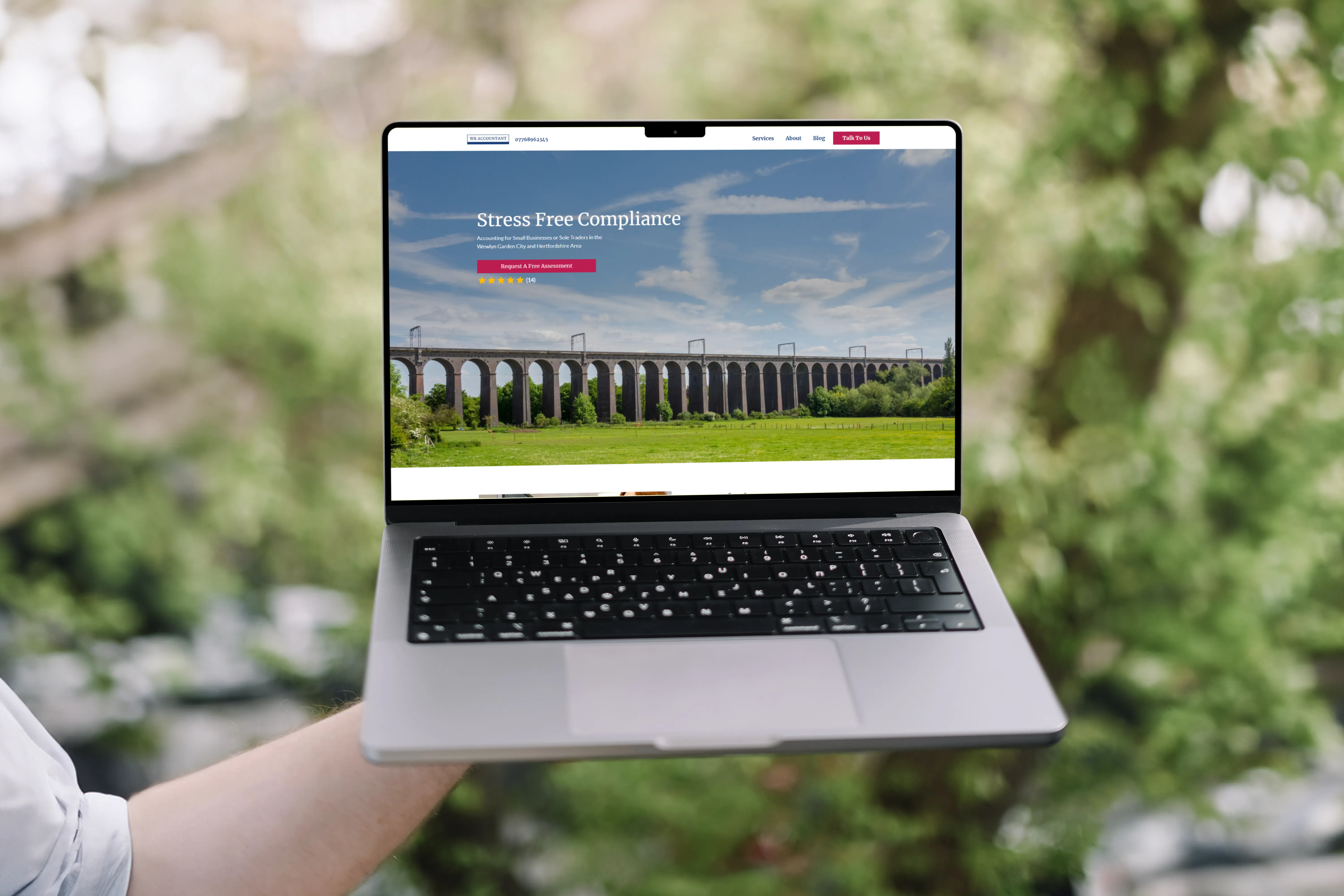 In a garden, a person holds up a laptop with a website displayed.